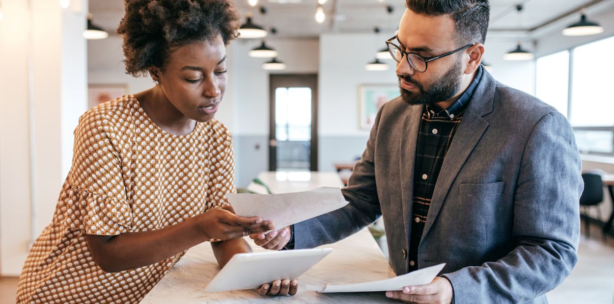 A woman and a man are standing at a table looking at papers.